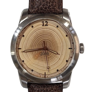 May include: A silver wristwatch with a brown leather band. The watch face is made of wood with a tree ring pattern and the numbers 12 and 2008.