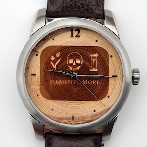 May include: A silver wristwatch with a brown leather strap. The watch face is made of wood with a skull, flower, and hourglass design. The text "Memento Mori" is engraved on the wood.