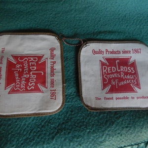 May include: Two vintage red and white pot holders with the text "Red Cross Stoves, Ranges & Furnaces" and "Quality Products since 1867".