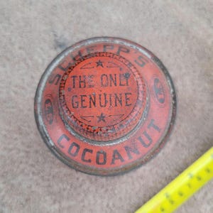 May include: Vintage Schepp's Cocoa Nut tin lid. The red lid features the text "THE ONLY GENUINE COCOANUT" in black lettering. The lid has a circular design with a star and decorative border. The tin shows signs of age and wear.