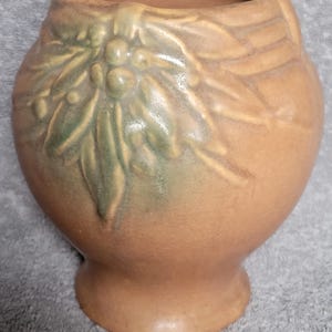 May include: A brown ceramic vase with a green floral design. The vase has a wide mouth and a rounded body.