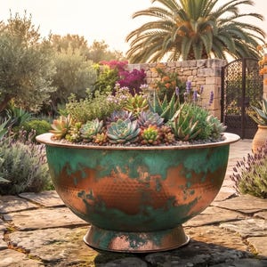 May include: A large, round, hammered copper bowl planter with a pedestal base, featuring a distinct patina finish with mottled teal and green oxidation over a warm metallic copper surface, filled with a variety of green and purple succulents.