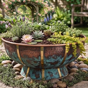 Puede incluir: Una maceta grande y redonda de cobre martillado con un acabado de pátina azul verdosa y tiras metálicas verticales de color latón. El recipiente en forma de cuenco se asienta sobre una base de pedestal y contiene suculentas, lavanda y un nenúfar.