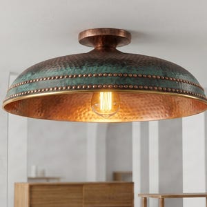 May include: A dome-shaped flush mount ceiling light fixture featuring a hammered copper exterior with a teal patina finish on the upper section. The rim is accented with a row of small metal studs and a smooth brass-toned edge, housing one bulb.