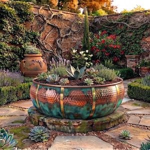 May include: A large, round, hammered copper planter with a teal patina finish and vertical brass bands, filled with various succulents. The planter sits on a circular stone base in a garden setting with terracotta pots and stone pavers.