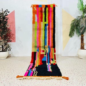 May include: A vibrant, rectangular rug with a colorful, abstract design. Vertical stripes in shades of orange, pink, green, blue, and black create a bold pattern. The rug has a textured appearance and is likely made of woven material. The rug is approximately 60 inches long.