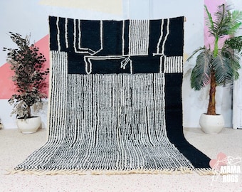 May include: Black and white geometric patterned rug with a fringe. The rug features a combination of vertical stripes and abstract shapes. The rug is made of a thick, woven material, and is displayed against a neutral background.