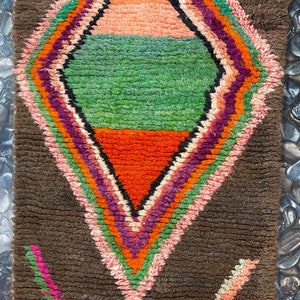 May include: A brown rug with a colorful diamond pattern in the center. The diamond is made up of stripes of pink, orange, green, and purple.