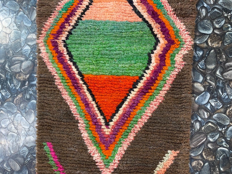 May include: A brown rug with a colorful diamond pattern in the center. The diamond is made up of stripes of pink, orange, green, and purple.