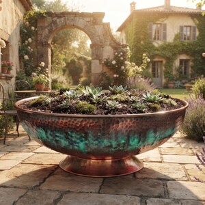 May include: A large, round, hammered copper planter bowl with a pedestal base, featuring a distinct teal-coloured patina finish on the lower exterior. The bowl is filled with dark soil and a variety of small green succulent plants.