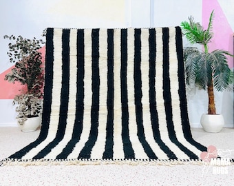 May include: A large, rectangular rug with a bold black and white striped pattern. The rug has a thick, textured pile and a fringed edge. The design is modern and graphic, suitable for a living room or bedroom.