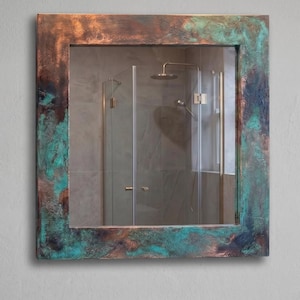 May include: A square wall mirror featuring a wide, flat frame with a weathered, oxidised finish. The frame displays a mottled blend of metallic copper, dark brown, and vibrant turquoise green tones, creating a textured, aged appearance.