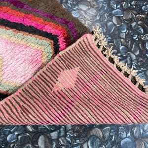 May include: A pink and brown striped rug with a fringe border. The rug is folded in half, revealing a pink and brown geometric pattern on the other side.