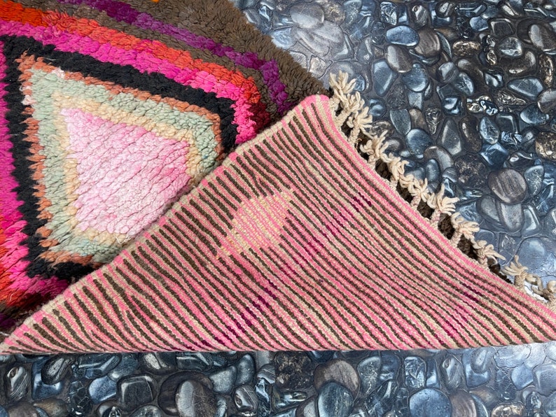 May include: A pink and brown striped rug with a fringe border. The rug is folded in half, revealing a pink and brown geometric pattern on the other side.