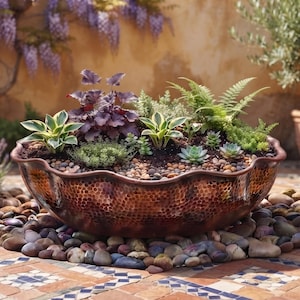 May include: A large, round, hammered copper bowl with a scalloped rim, filled with a variety of green and dark purple succulent plants and small stones. The bowl has a metallic, textured finish and sits on a bed of smooth, multi-coloured river rocks.