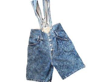 May include: Acid-wash blue denim overalls featuring a high-waisted design with a button-front closure. The garment includes two shoulder straps and a light-colored patterned fabric lining visible at the top waistline and inside the straps.
