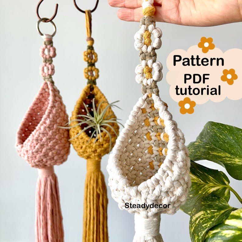 K&ouml;nnte beinhalten: Drei Makramee-Pflanzenh&auml;nger mit Blumendesign. Die H&auml;nger sind aus nat&uuml;rlichem Baumwollschnur hergestellt und haben unten einen Quasten. Die H&auml;nger sind in Pink, Gelb und Wei&szlig;. Das Bild enth&auml;lt den Text "Pattern PDF tutorial".