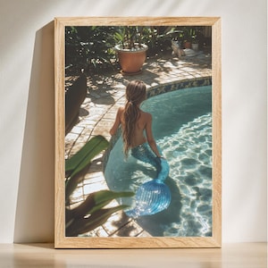 May include: A mermaid with long blonde hair sits in a swimming pool with a blue tail. The pool is surrounded by a tiled patio and lush green plants.