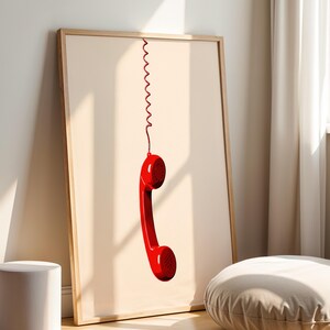 May include: A framed print of a red rotary phone handset hanging by a coiled cord against a light beige background.
