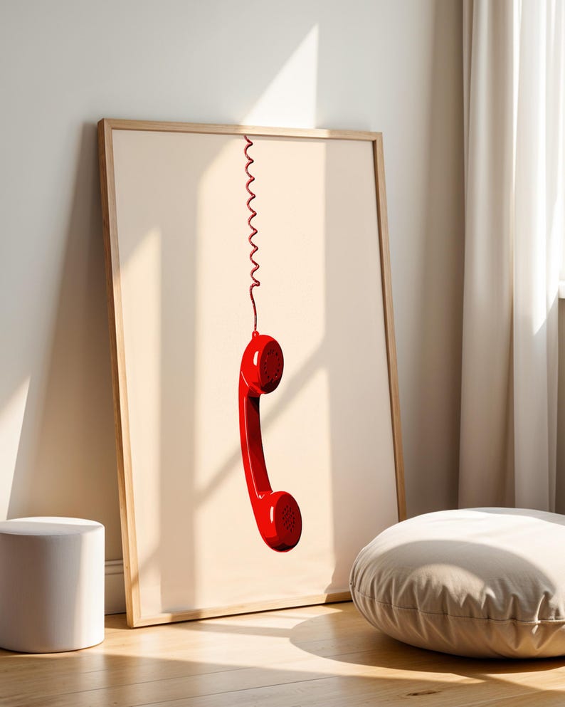 May include: A framed print of a red rotary phone handset hanging by a coiled cord against a light beige background.