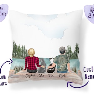 Op de afbeelding: Een gepersonaliseerd kussen met een aquarel-illustratie van een stel en twee honden die op een steiger zitten met uitzicht op een meer. De namen "Sophie", "Ollie", "Tia" en "Rick" staan onder de figuren. Het kussen is aanpasbaar met maximaal 300 verschillende hond- en kat-avatars.