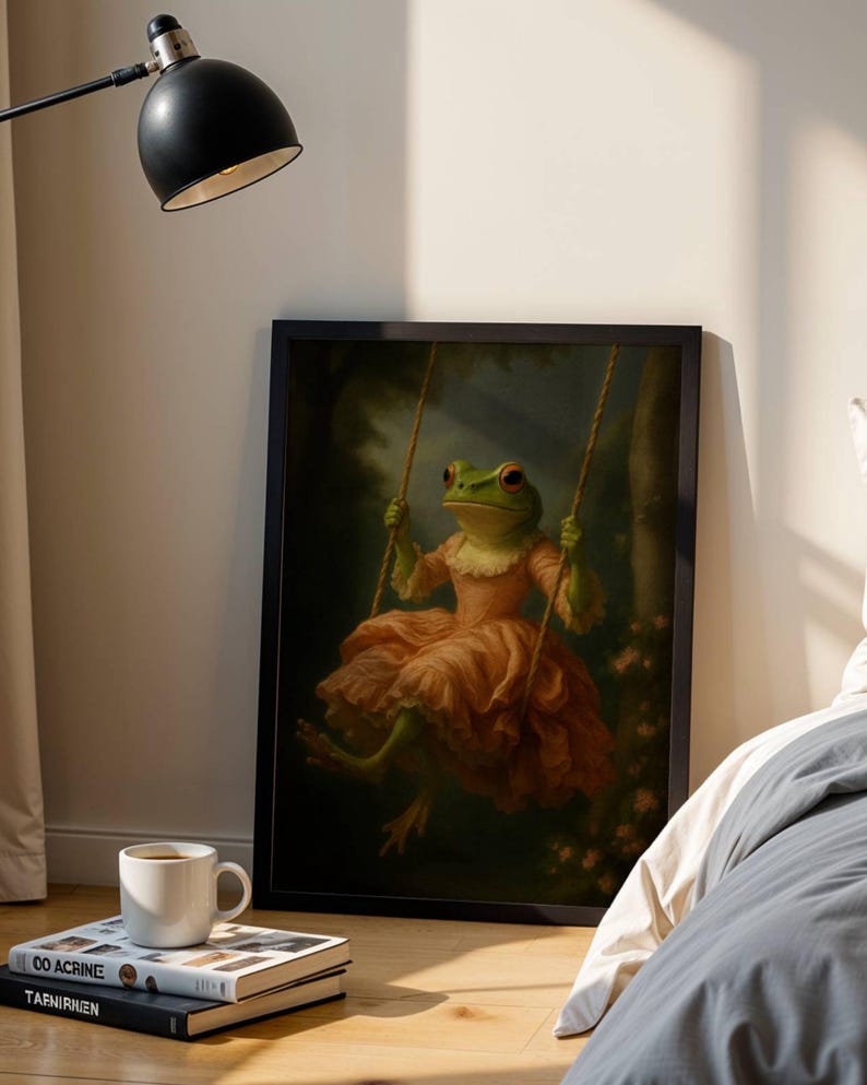 May include: A framed art print depicts a green frog in a peach-colored dress on a swing. The frog is in a forest setting with pink flowers. The artwork is displayed on a wooden floor next to a bed and a lamp.