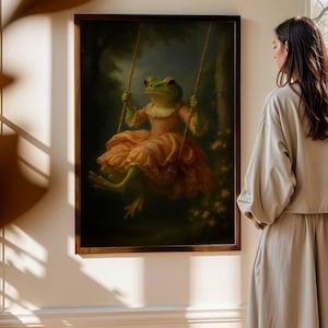 May include: A framed artwork depicts a frog in a pink dress on a swing. The frog has green skin and red eyes. The artwork is set in a forest scene with a dark background and is framed in a dark wood frame.