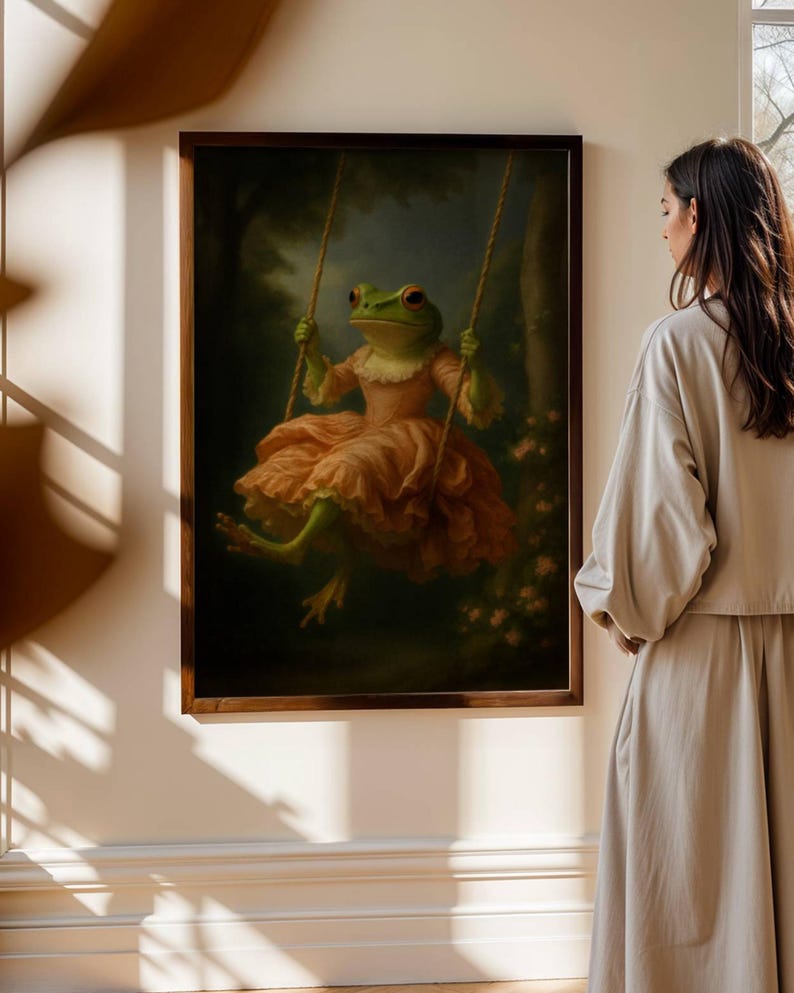 May include: A framed artwork depicts a frog in a pink dress on a swing. The frog has green skin and red eyes. The artwork is set in a forest scene with a dark background and is framed in a dark wood frame.