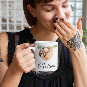 May include: White ceramic mug featuring a sloth hanging from a branch, wearing a floral crown, with the name "Madison" printed below.