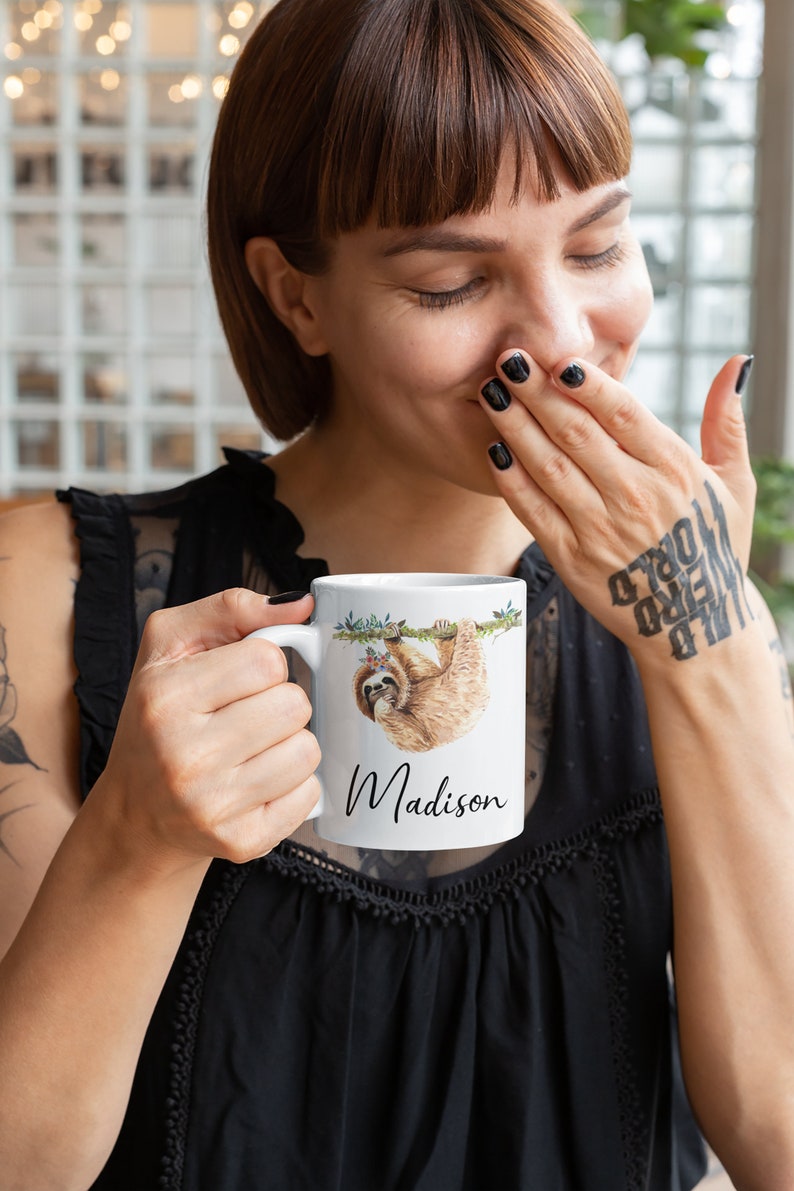 May include: White ceramic mug featuring a sloth hanging from a branch, wearing a floral crown, with the name "Madison" printed below.