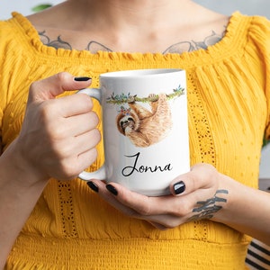 May include: White ceramic mug featuring a watercolour illustration of a sloth hanging from a branch. The sloth is wearing a flower crown. The mug is personalised with the name "Jonna" written in black cursive.