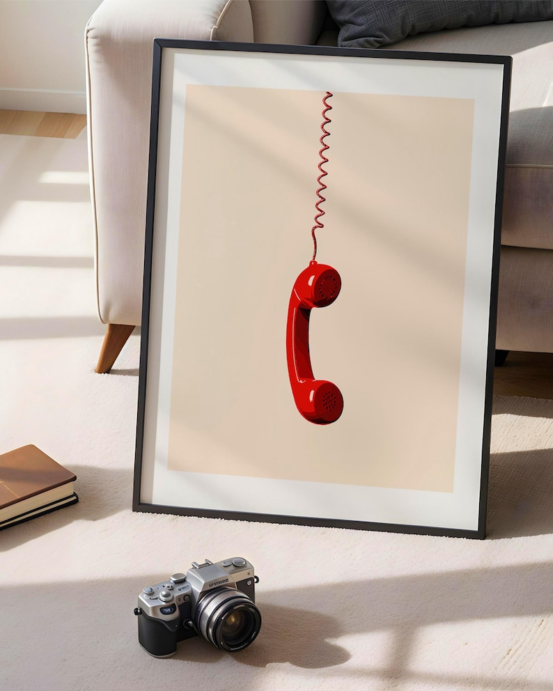 May include: A framed print of a red rotary phone handset hanging by a coiled cord against a light beige background.