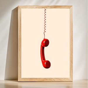 May include: A framed print of a red rotary phone handset hanging by a coiled cord against a light beige background.