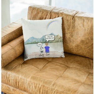 May include: A white throw pillow with a watercolor illustration of a person and a dog sitting on a dock overlooking a lake. The sky is blue with a rainbow and the text "They still talk about you" is in a speech bubble. The dog is named Marty and the person is named Levi.