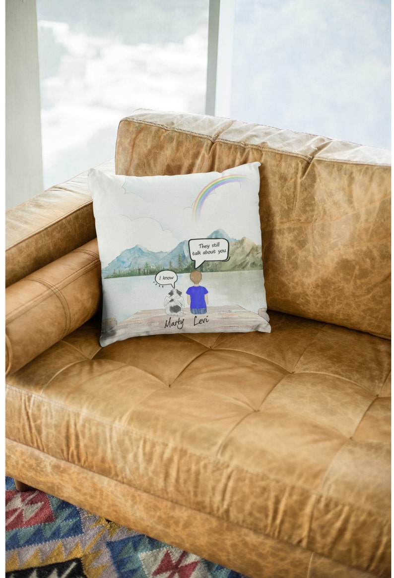 May include: A white throw pillow with a watercolor illustration of a person and a dog sitting on a dock overlooking a lake. The sky is blue with a rainbow and the text "They still talk about you" is in a speech bubble. The dog is named Marty and the person is named Levi.
