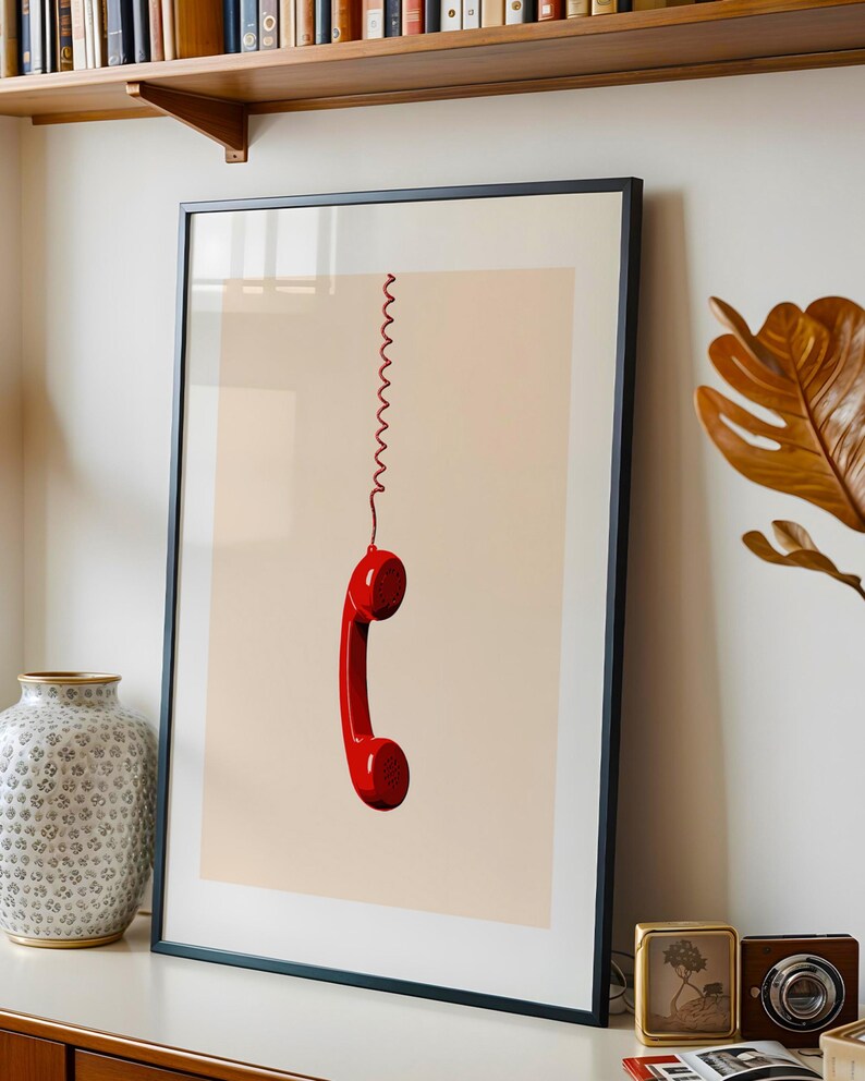 May include: A framed print of a red rotary phone receiver hanging by a coiled cord against a light beige background.