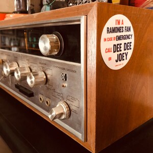 May include: A vintage wooden stereo receiver with a silver faceplate and a sticker that reads "I'm a Ramones fan. In case of emergency call Dee Dee or Joey."