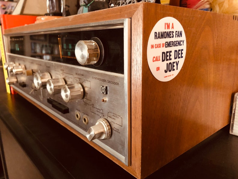 May include: A vintage wooden stereo receiver with a silver faceplate and a sticker that reads "I'm a Ramones fan. In case of emergency call Dee Dee or Joey."