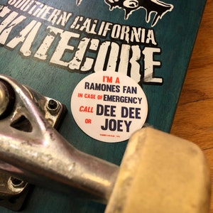 May include: A blue skateboard with a white skull graphic and the text "Southern California Katecrore". A white sticker with red and blue text reads "I'm a Ramones Fan In Case of Emergency Call Dee Dee or Joey".