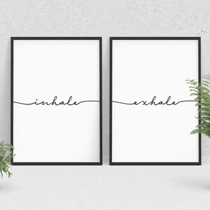 May include: Two black framed prints with white backgrounds. The left print has the word "inhale" written in black cursive. The right print has the word "exhale" written in black cursive.
