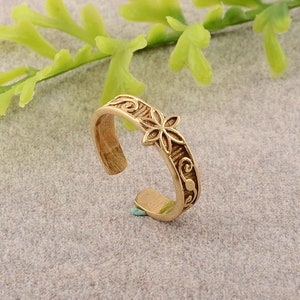 Può includere: Anello per dita dei piedi regolabile dorato con un design floreale. L'anello presenta un delicato design floreale al centro e un motivo a scorrimento attorno alla fascia.