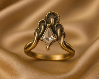 Op de afbeelding: Een goudkleurige ring met een heldere, ruitvormige middensteen. De ring heeft een uniek ontwerp met paddenstoelachtige accenten en gebogen banden. De ring is geplaatst tegen een gouden, getextureerde achtergrond.