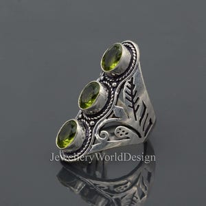 May include: A silver ring featuring three green gemstones and an elaborate floral design.