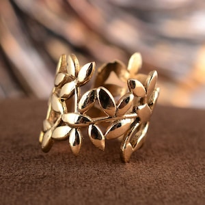 May include: A gold leaf ring featuring a delicate design of leaves and branches. The ring is made of metal and has a smooth finish.