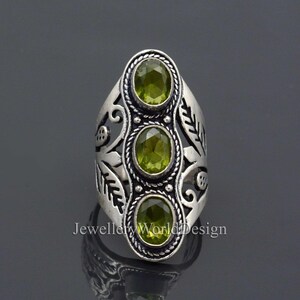 May include: Silver ring with an ornate design featuring three green gemstones. The ring has a leaf motif and is set with three round, faceted stones.
