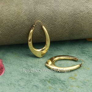 May include: A pair of gold-coloured, teardrop-shaped hoop earrings. The earrings have a smooth, polished surface and a simple, elegant design. The text "Jewellery WorldDesign" is visible at the bottom of the image.