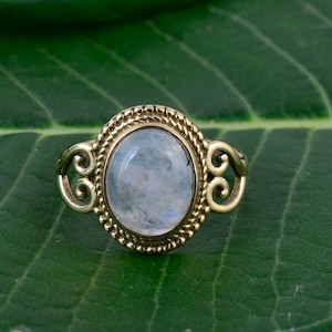 Puede incluir: Un anillo de oro con una gran piedra de luna ovalada engastada en un diseño de filigrana.