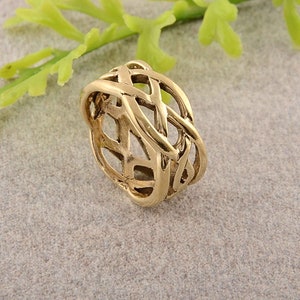 Può includere: Un anello dorato con un designo a nodo celtico. L'anello è fatto di un metallo spesso e intrecciato.