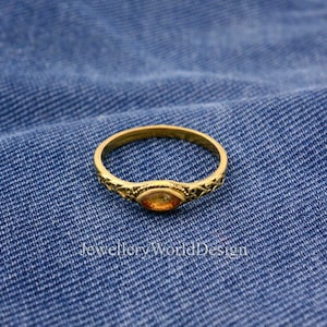 Peut inclure: Une bague en or avec un design délicat et orné et une seule pierre précieuse orange de forme ovale au centre.