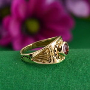 May include: A gold ring with a red gemstone set in a decorative design.